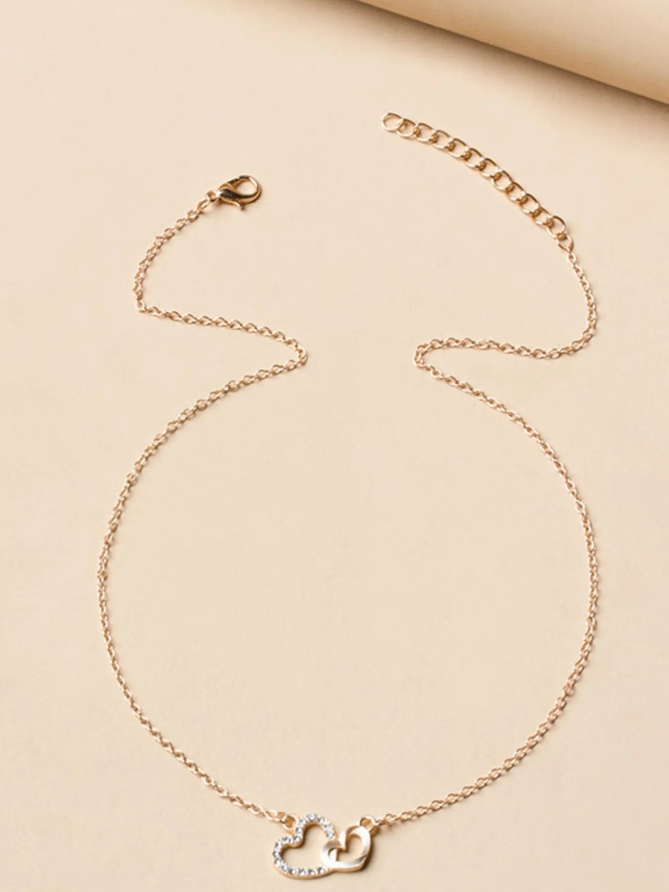 Gold Double Heart Pendant Necklace displayed on beige background, featuring zircon-studded and polished heart charms.