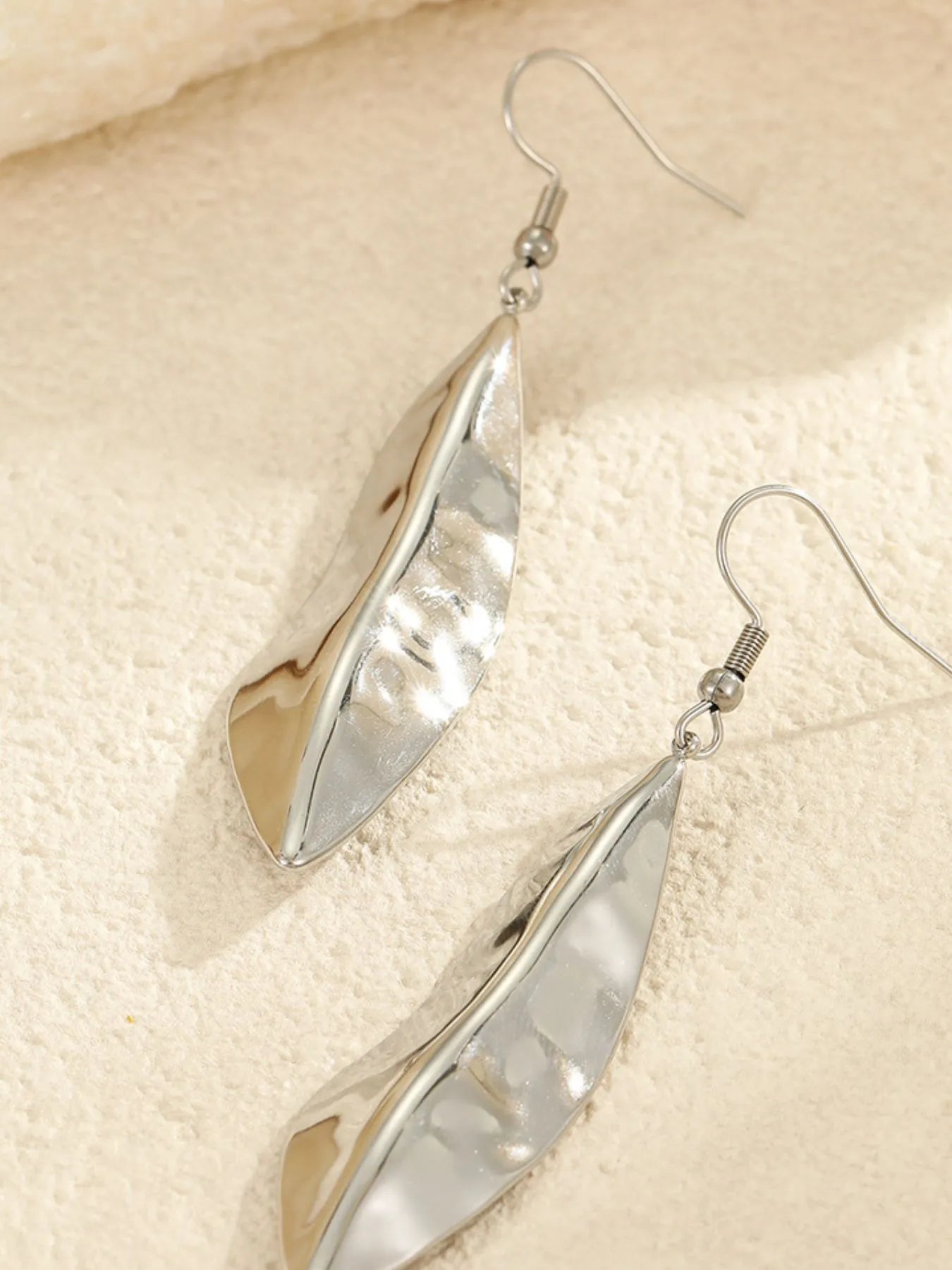 Silver feather drop earrings with a reflective, sculpted texture, offering a sleek and modern jewelry option for casual or dressy looks.