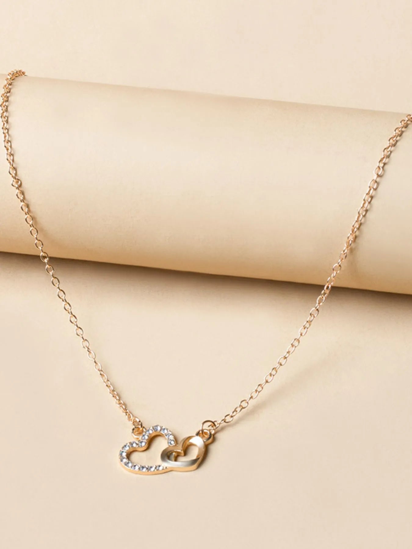 Elegant Double Heart Pendant Necklace with 18K gold-plated chain and intertwined hearts, styled on a rolled paper backdrop.