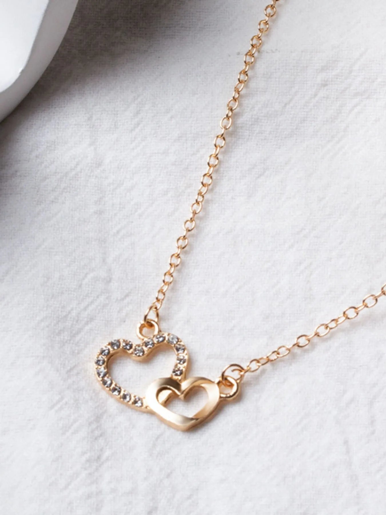 Close-up of Double Heart Pendant Necklace on fabric, highlighting zircon-studded and smooth gold heart charms.