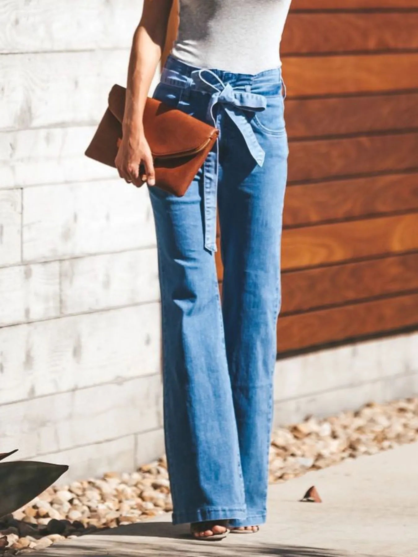 Women's Tie-Front Flare Jeans styled with a brown clutch and sleeveless top, showcasing a trendy high-rise and wide-leg cut.