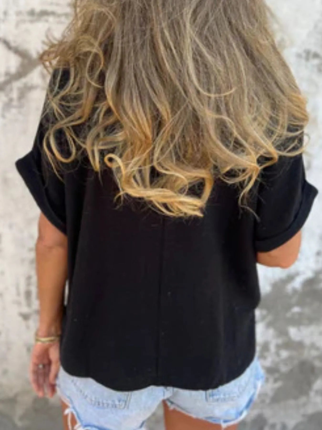Back view of black Women's Oversized Essential Tee showcasing its relaxed drape and soft fabric, paired with denim shorts.