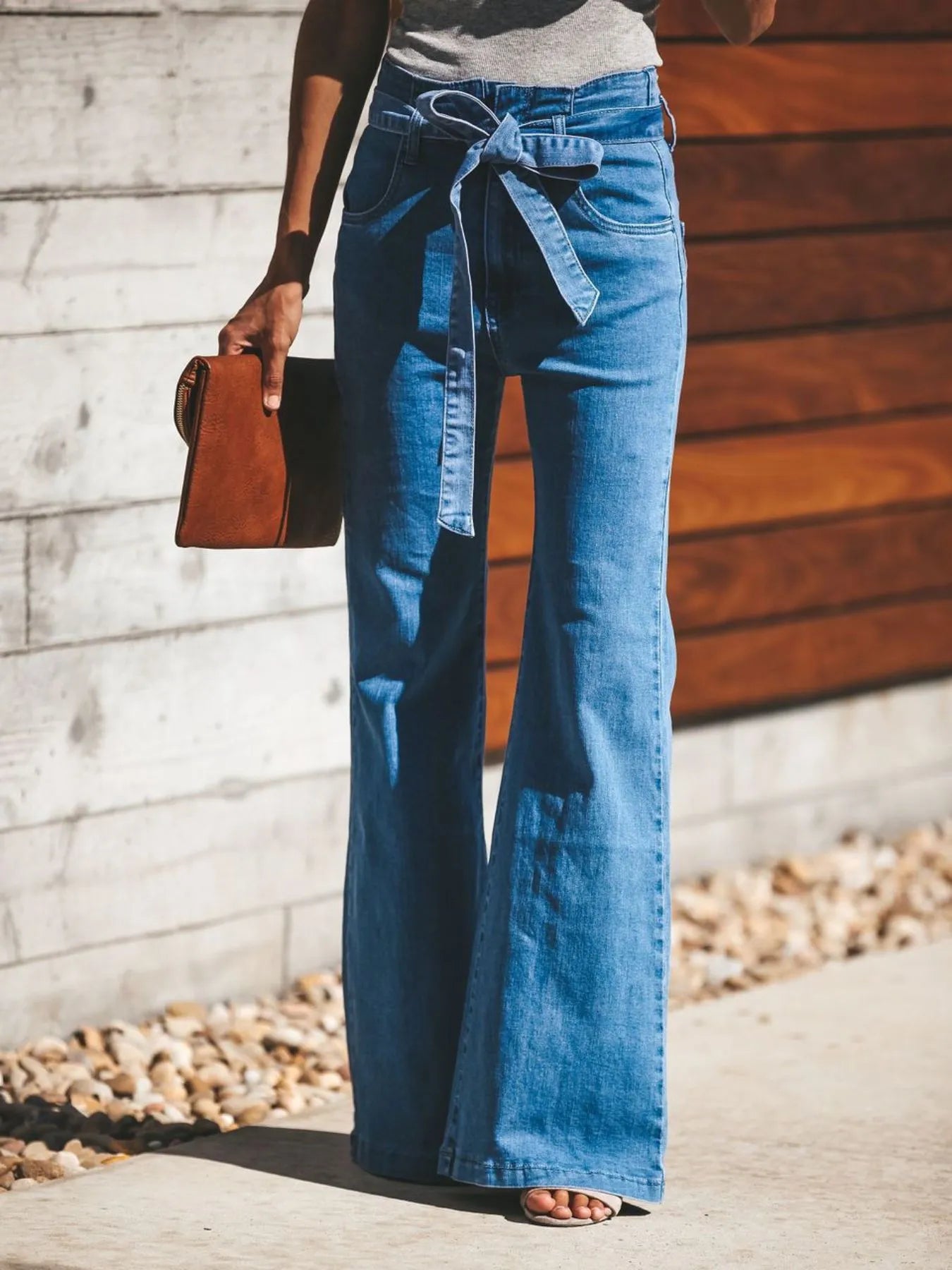Women's Tie-Front Flare Jeans in light blue denim with high waist and wide-leg silhouette, styled with a sleeveless top and clutch bag.