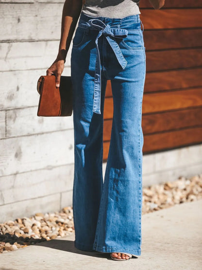 Women's Tie-Front Flare Jeans in light blue denim with high waist and wide-leg silhouette, styled with a sleeveless top and clutch bag.