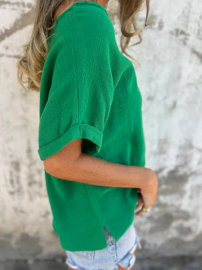 Side view of green Women's Oversized Essential Tee featuring rolled sleeves and side slit hem, styled with denim shorts.