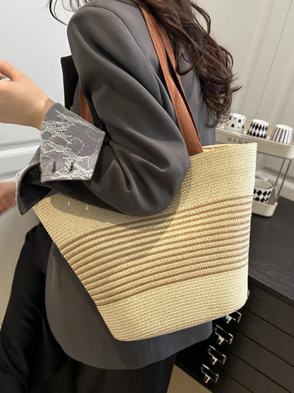 Striped woven medium size tote bag in cream and tan, worn with gray blazer. Fashionable shopper bag for work or leisure.
