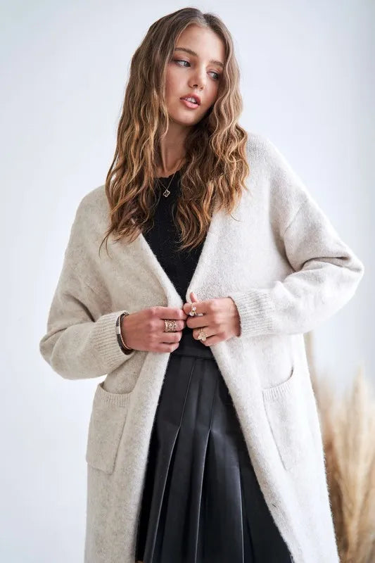 Two-tone open cardigan by Adora in beige, styled with a black top and pleated skirt for a cozy yet chic layered look.