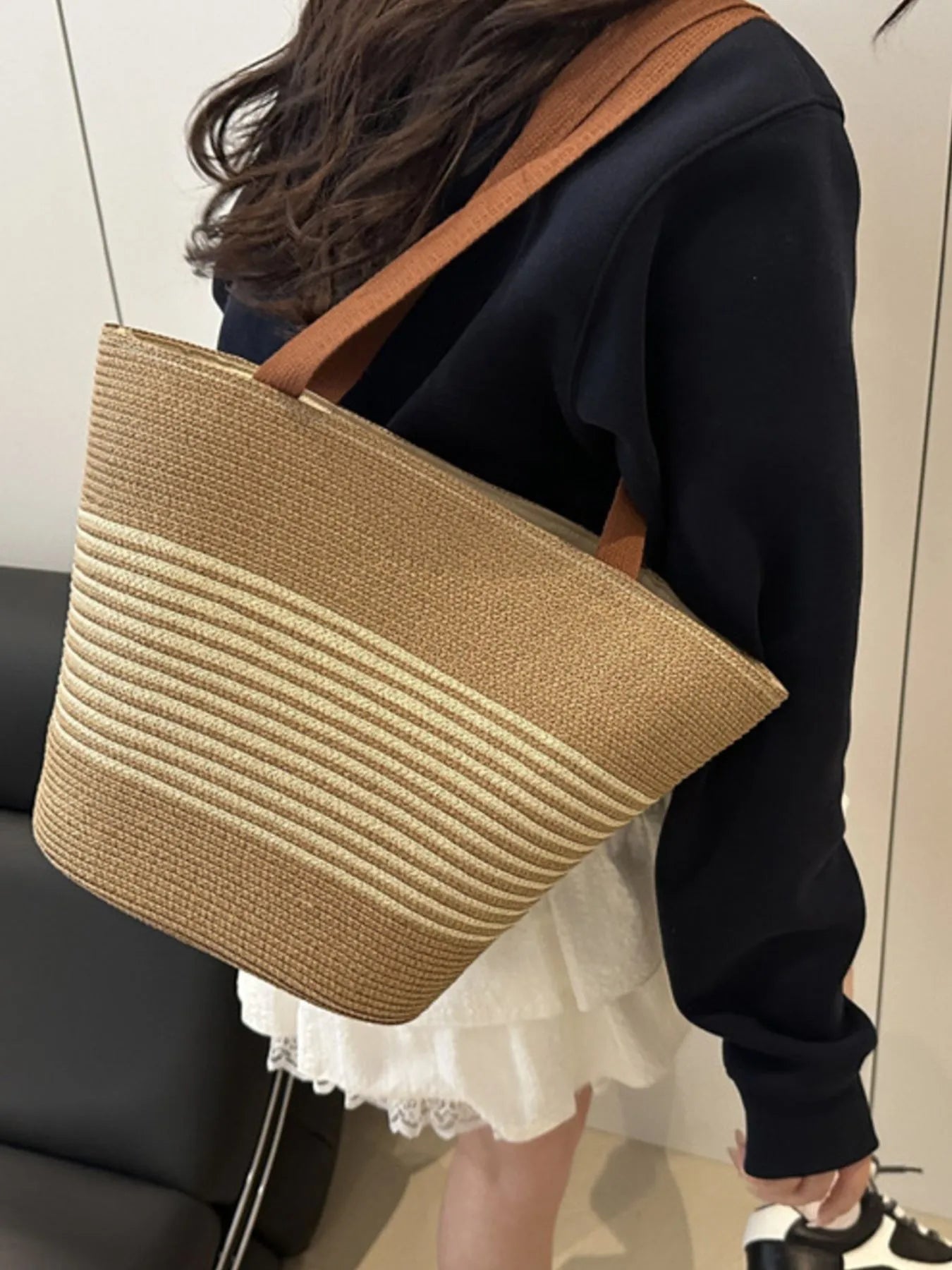 Striped woven medium size tote bag in beige and cream, worn over shoulder with black hoodie and white skirt. Perfect for casual wear.