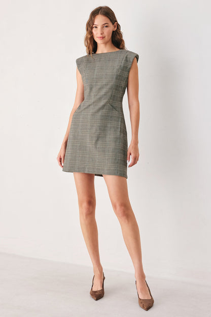 A woman modeling a sleeveless, knee-length olive green plaid dress with structured shoulders, paired with brown pointed-toe heels, against a plain white studio background.