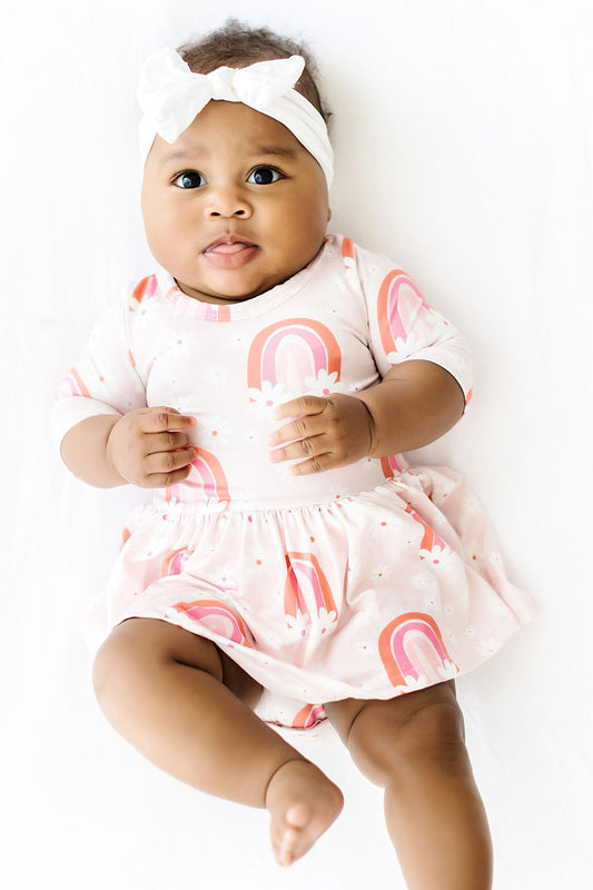 Baby wearing a white romper with pink rainbow patterns on a white background