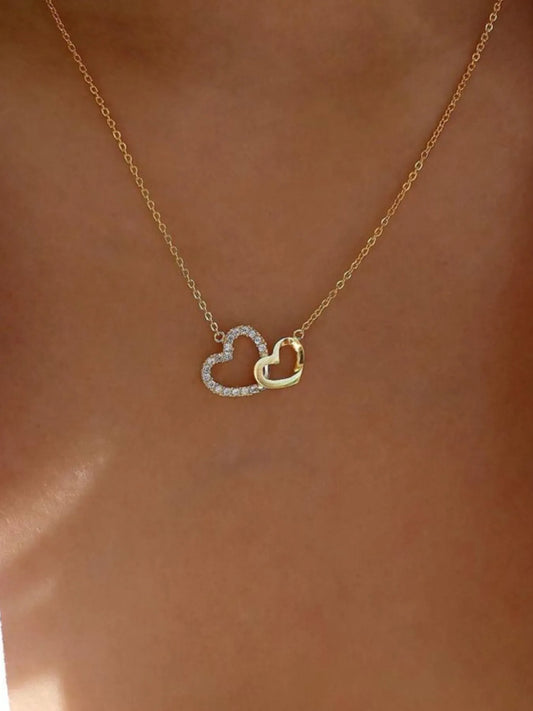 Double Heart Pendant Necklace with gold chain and intertwined hearts, one encrusted with zircon stones, worn on a model's neck.