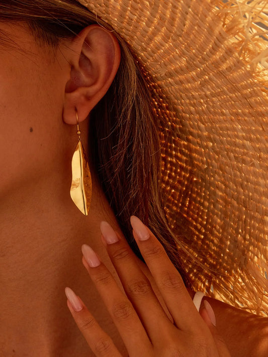 Gold feather drop earrings worn with a straw hat, showcasing their lightweight, elegant design perfect for summer accessories.