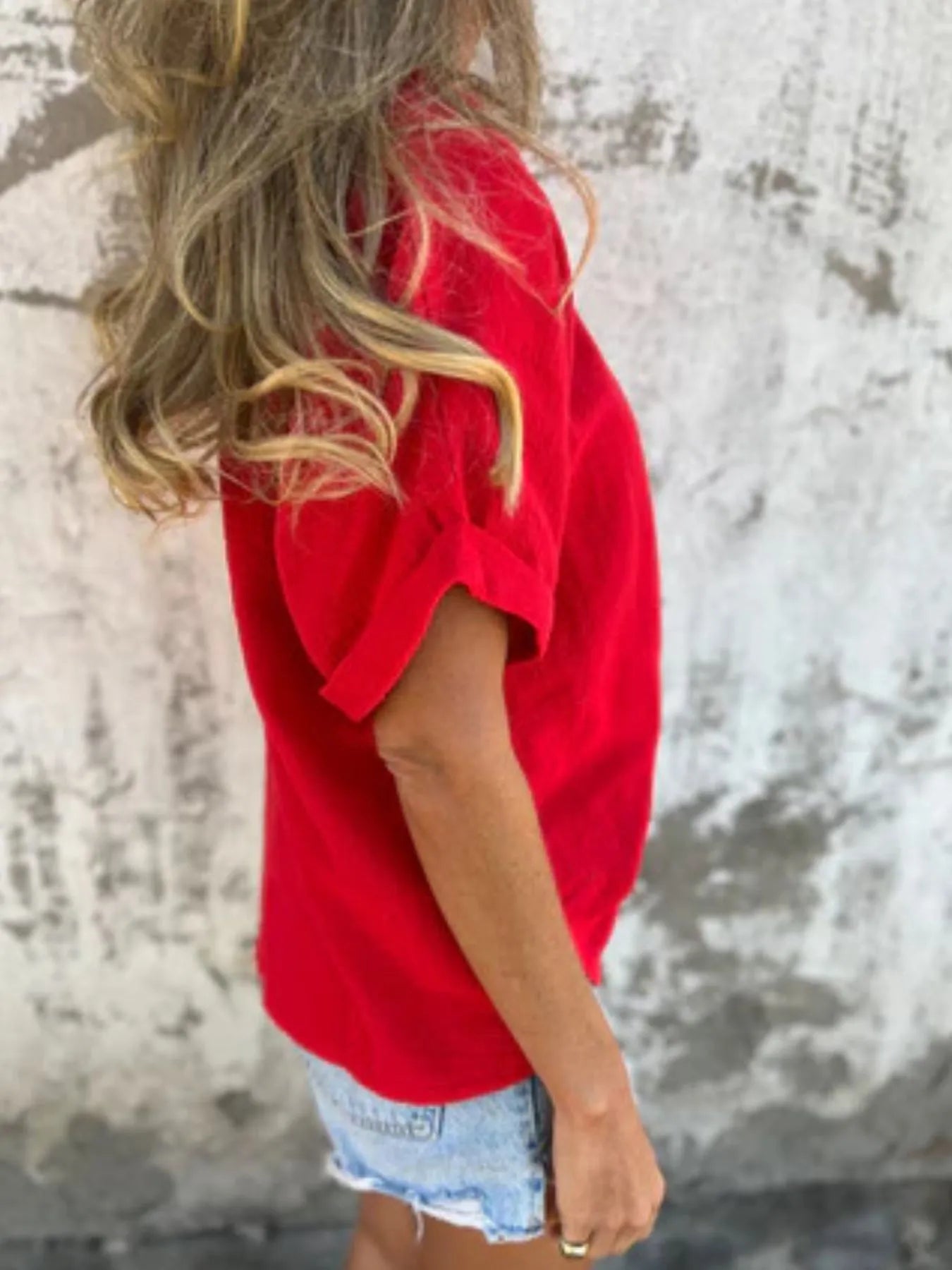 Side profile of red Women's Oversized Essential Tee with casual rolled sleeves and curved hem, styled for comfort and ease.
