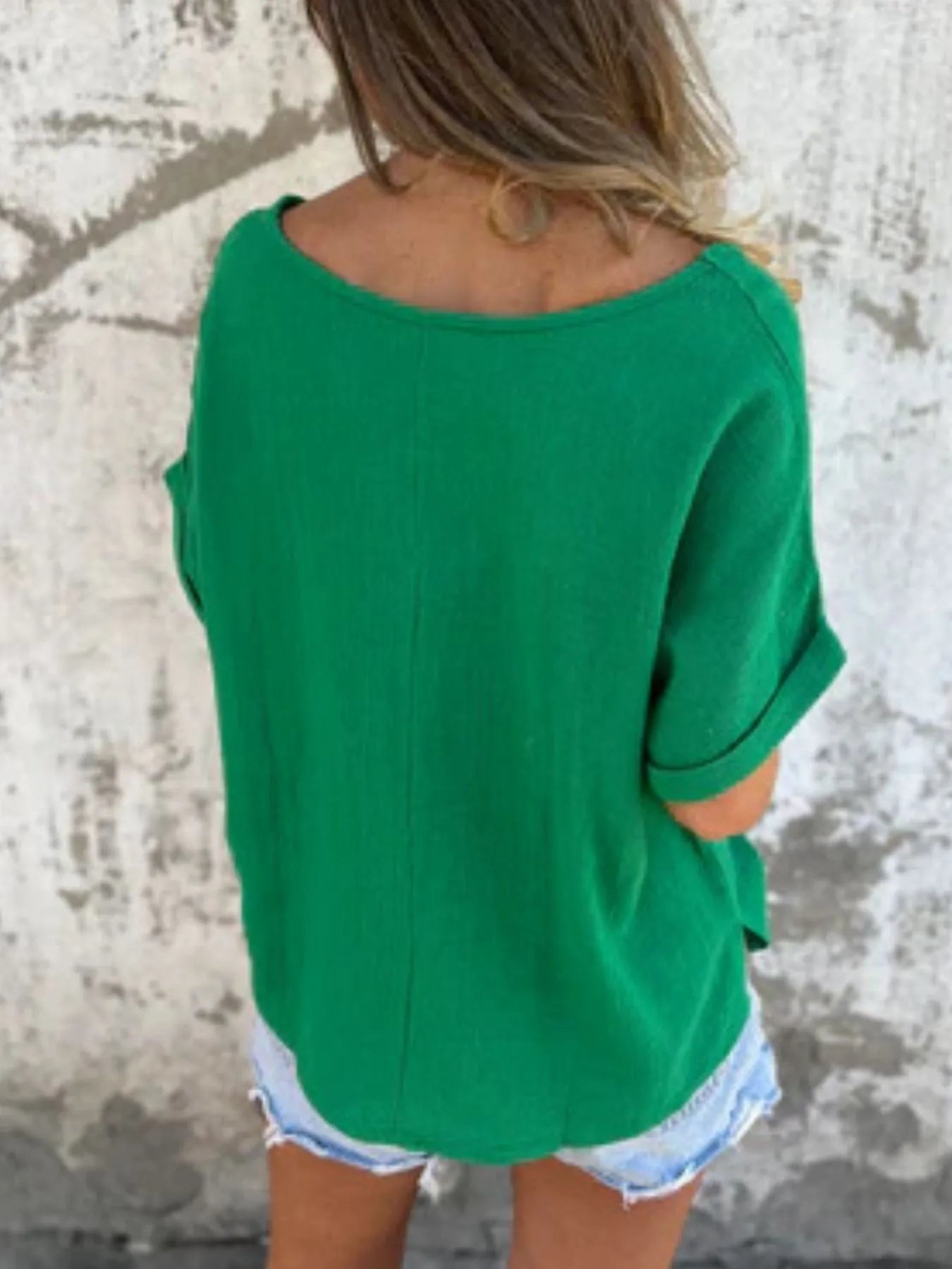 Back view of green Women's Oversized Essential Tee showing curved hem and loose fit, styled with casual denim shorts.